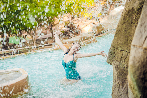 Young woman relaxing under a waterfall in aquapark. Vacation concept