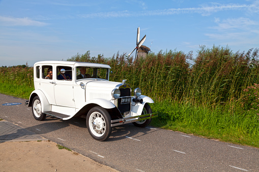 Kinderdijk, Netherlands - August 26 2017: Newly wed couple driven in an old white 1929 Model A Ford Town Sedan with a windmill behind.