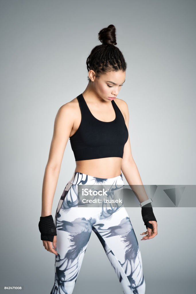 Powerful afro american young woman in sports wear, studio shot Attractive afro amercian young woman in sports wear standing against grey background, studio shot. Gray Background Stock Photo