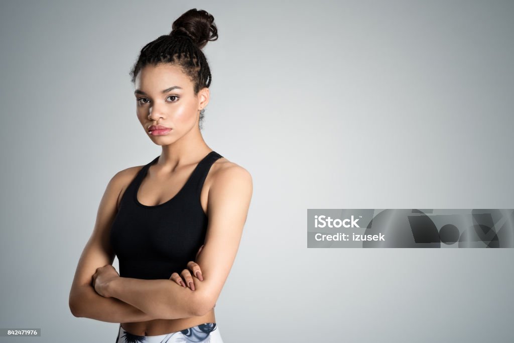 Fitness young woman in sports wear, studio shot Attractive afro amercian young woman in sports wear standing with arms crossed against grey background, studio shot. Teenager Stock Photo