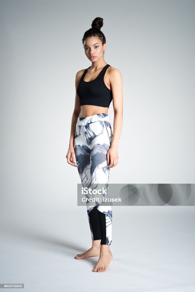 Cute afro american young woman in sports wear, studio shot Full length of attractive young woman in sports wear standing against grey background, studio shot. Hair Bun Stock Photo