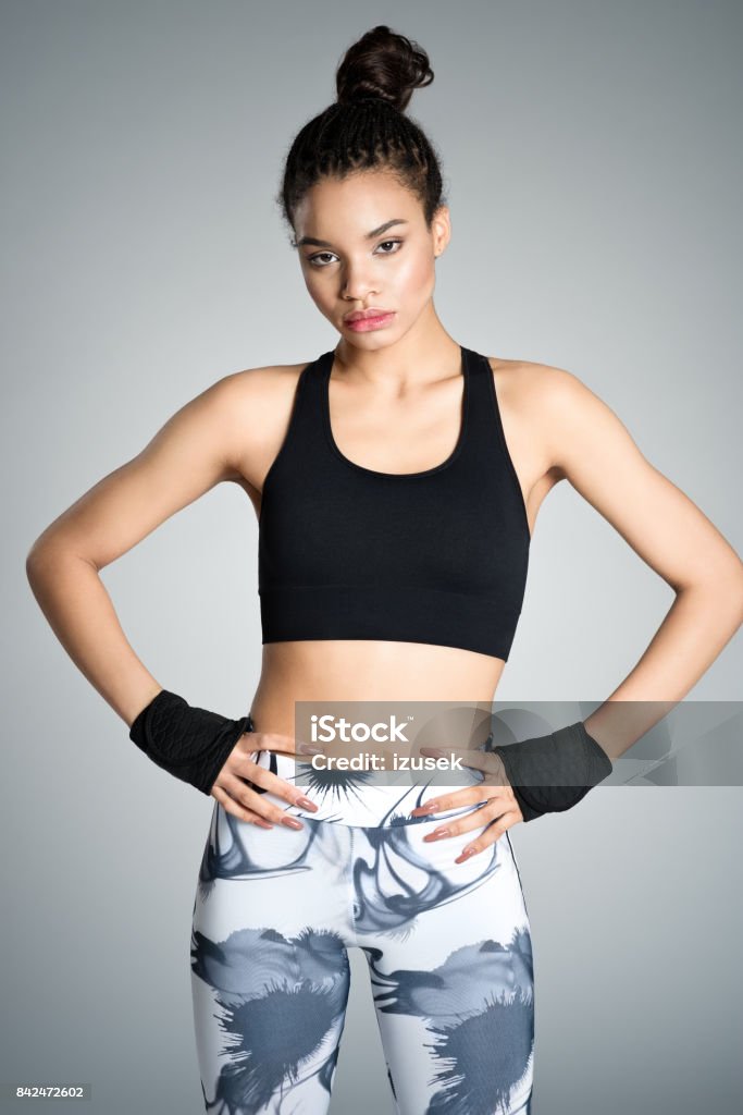 Fitness young woman in sports wear, studio shot Attractive afro amercian young woman in sports wear standing with hands on hips against grey background, studio shot. 16-17 Years Stock Photo