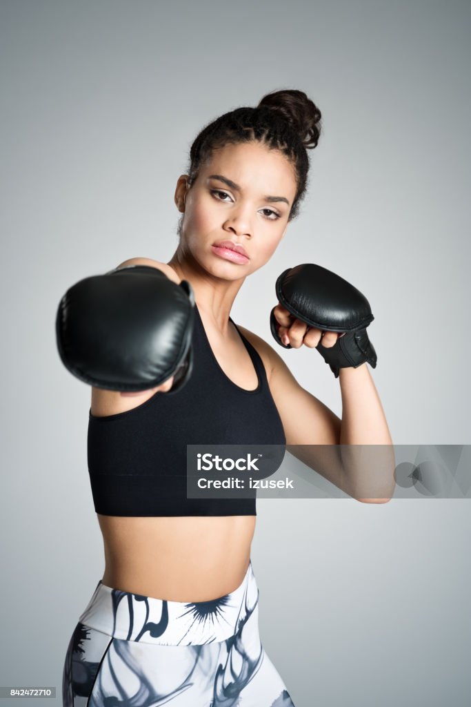 Attractive fit young woman boxing, studio shot Attractive fit young woman wearing sports clothes boxing. Studio shot, grey background. Boxing Glove Stock Photo