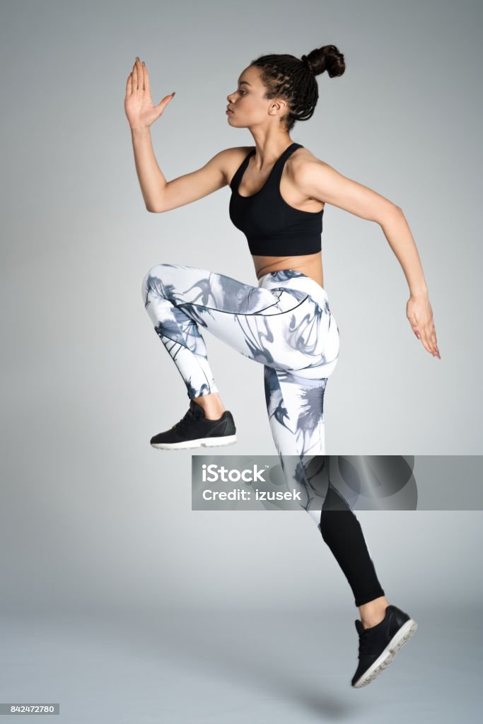 Afro american young woman in sports wear jumping, studio shot Attractive afro amercian young woman in sports wear jumping against grey background, studio shot. Sport Stock Photo