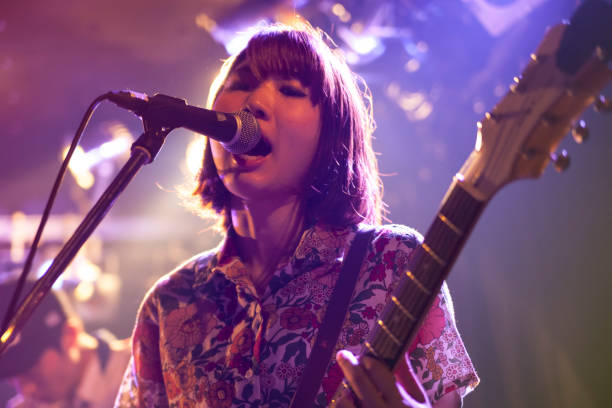 Woman Playing The Guitar A young Japanese woman is playing the guitar during a live band event. string ensemble stock pictures, royalty-free photos & images