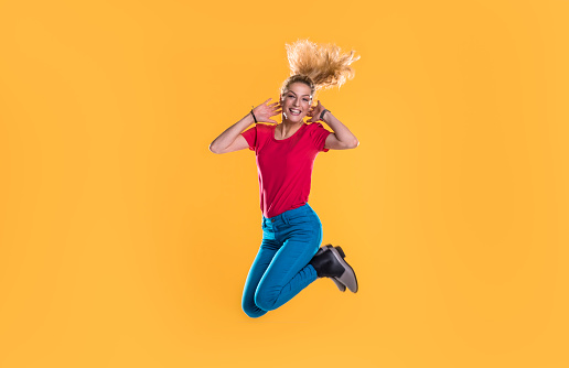 Happy woman jumping in front of the yellow background in the studio