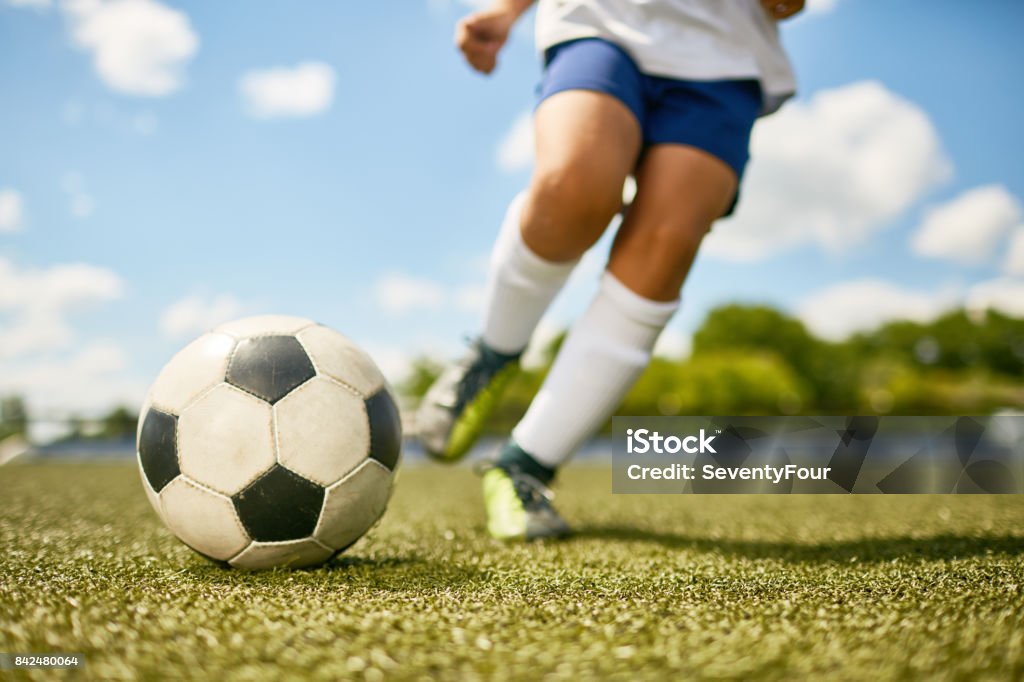 Boy Kicking Ball Low section portrait of unrecognizable teenage boy kicking ball during football practice in field Soccer Stock Photo