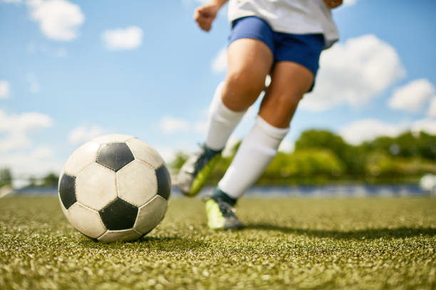 Boy Kicking Ball Low section portrait of unrecognizable teenage boy kicking ball during football practice in field kicking stock pictures, royalty-free photos & images