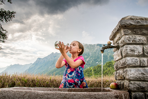 Girl Filling Bottle With Water At The Mountain Village Faucet