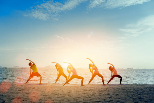 giovane gruppo uomo e donna pratica yoga sul rilassamento del tappetino in allenamento di classe con pose fitness sport per la salute sulla spiaggia e mare città moderna all'alba relax vacanza vacanza in estate. - yoga exercising outdoors group of people foto e immagini stock