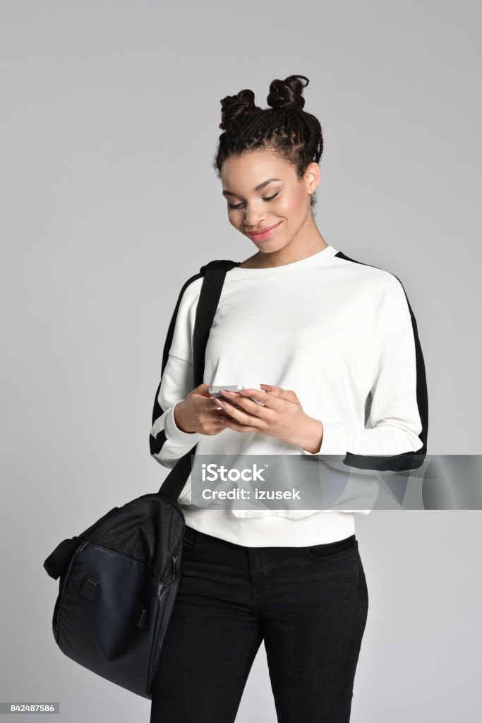 Smiling afro american teen student using smart phone Studio portrait of smiling afro american teen female student using smart phone. Studio shot, grey background. Mobile Phone Stock Photo