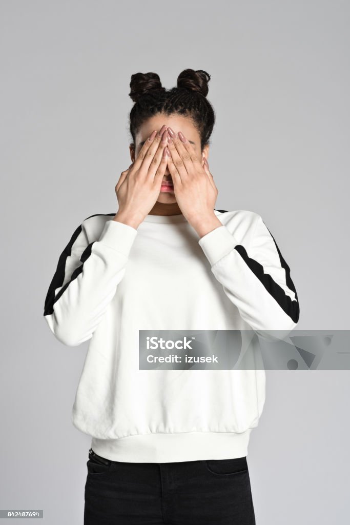 Afro american teenager woman covering eyes with hands Studio portrait of afro american teenage woman covering eyes with hands. Studio shot, grey background. 16-17 Years Stock Photo
