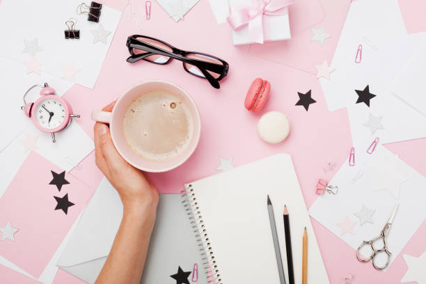 istock Female hand with coffee cup, macaron, office supply, gift and notebook on pastel desk top view. Fashion pink woman workplace background for blogging. Flat lay. 842487828