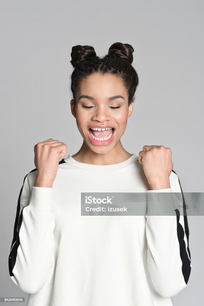 Happy afro american teenager girl Studio portrait of happy afro american teenage woman raising fists and smiling. Studio shot, grey background. 16-17 Years Stock Photo