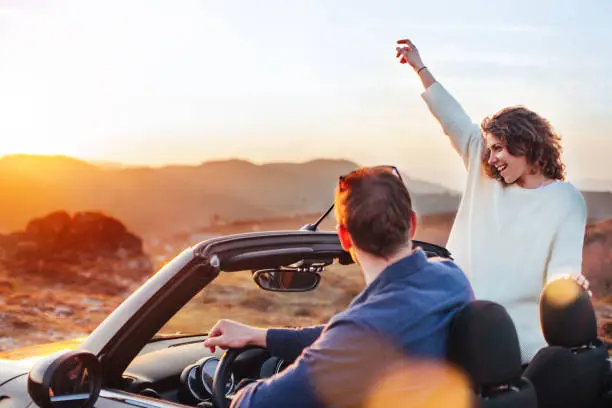 Photo of Happy couple looking at sunset from convertible