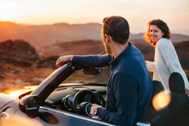 Photo of Happy couple looking at sunset from convertible