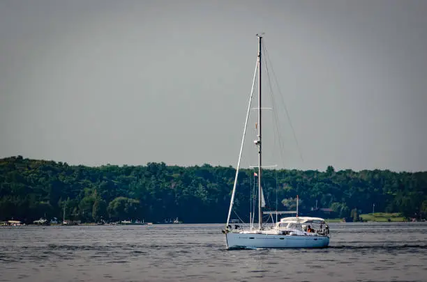 Sailboat motoring on the St. Lawrence River with the Upper New York State treed shoreline in the background.