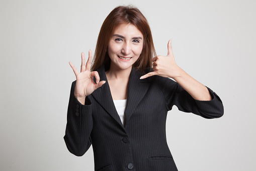 Young Asian woman show with phone gesture and OK sign on gray background