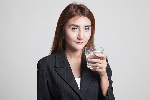 Young Asian woman with a glass of drinking water on gray background