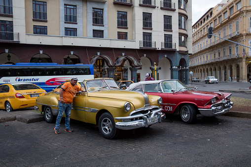Vintage cars are parking on the street. Incidental people on the background.