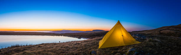 Yellow pyramid tent illuminated sunrise in idyllic mountain wilderness panorama