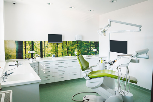 Empty brightly lit place of work of a dentist, modern dentist office with green dentist's chair, no people