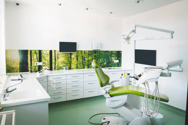 Dentist's chair in brightly lit clinic Empty brightly lit place of work of a dentist, modern dentist office with green dentist's chair, no people dentists chair stock pictures, royalty-free photos & images