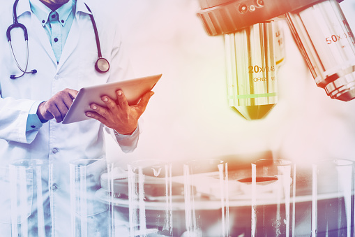 Medical science research and development concept - Doctor holding tablet computer with scientific instrument, microscope and  chemical test tube in lab background.