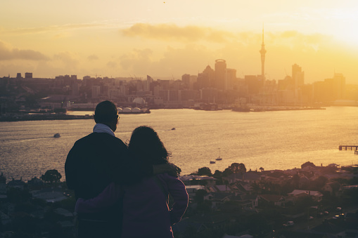 Happy senior couple watching sunset in Auckland city skyline with city center and Auckland Sky Tower in New Zealand.
