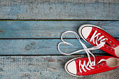 A pair of red retro sneakers on a blue wooden background, laces lined in a heart shape. Concept of young hipster love