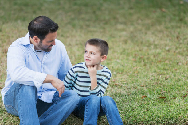 istock Father and young son sitting on grass, talking 842697034