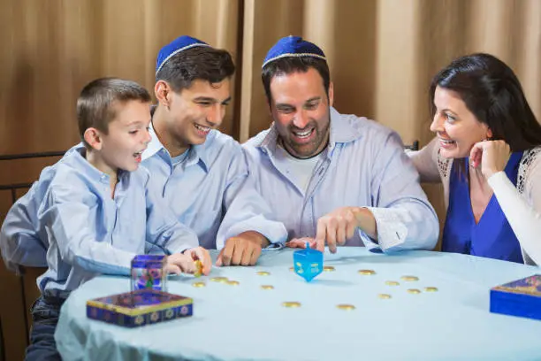 A jewish family of four sitting around a table playing a dreidel game. The younger boy is 7 years old and his brother is 13.