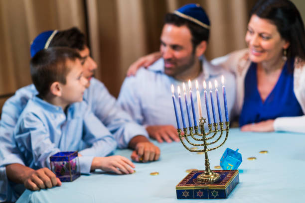 Family of four celebrating hanukkah A jewish family of four sitting around a table talking, out of focus in the background. The younger boy is 7 years old and his brother is 13. The focus is on the menorah in the foreground yarmulke photos stock pictures, royalty-free photos & images