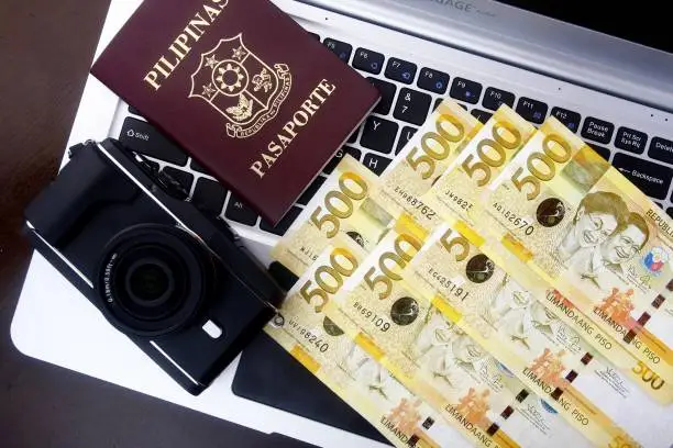 Photo of a camera, passport and Philippine peso bills on a laptop computer keyboard.
