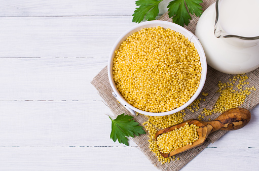 Raw organic millet and a jug of milk on a light wooden background. Selective focus.