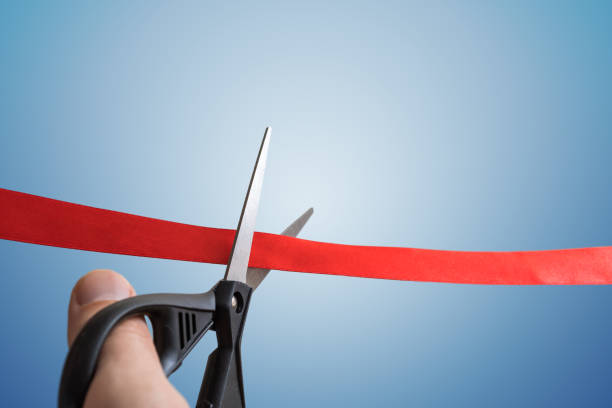 scissors are cutting red ribbon. opening ceremony concept. isolated on blue background. - business opening beginnings ribbon cutting imagens e fotografias de stock