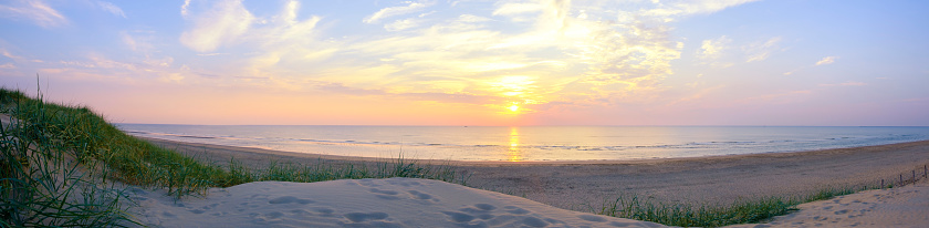 View from the dunes on the sand beach of the North Sea shore on the coast line in The Netherlands during a beautiful summer sunset after a warm day in August. Wide panoramic image.