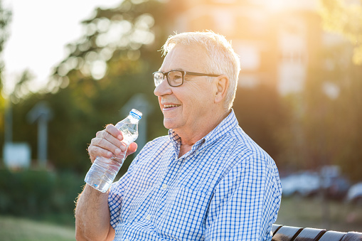 Outdoor portrait of senior man who is drinking water.