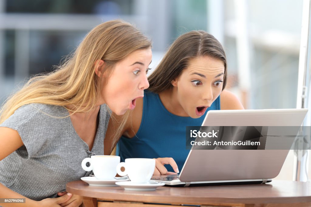 Amazed friends watching scandalous content in a bar Two amazed friends watching scandalous content in a laptop sitting in a bar Sale Stock Photo