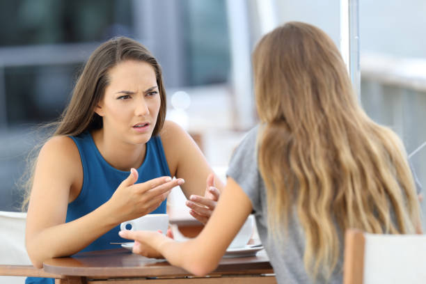 Two girls talking seriously in a coffee shop Two angry girls talking seriously sitting in a coffee shop sister stock pictures, royalty-free photos & images