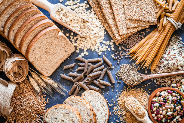 Dietary fiber food still life Top view of wholegrain and cereal composition shot on rustic wooden table. This type of food is rich of fiber and is ideal for dieting. The composition includes wholegrain sliced bread, wholegrain pasta, oat flakes, flax seed, brown rice, mixed beans, wholegrain crackers and spelt. Predominant color is brown. DSRL studio photo taken with Canon EOS 5D Mk II and Canon EF 100mm f/2.8L Macro IS USM rice cereal plant stock pictures, royalty-free photos & images