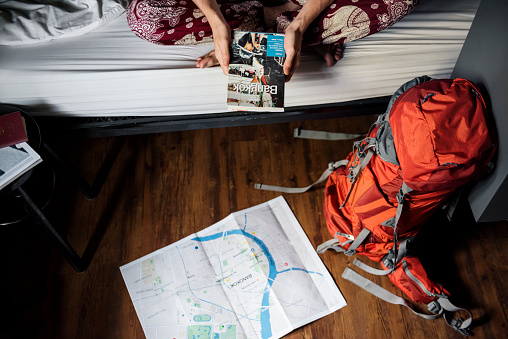 Hands holding Bangkok Thailand travel guide book with map on the floor