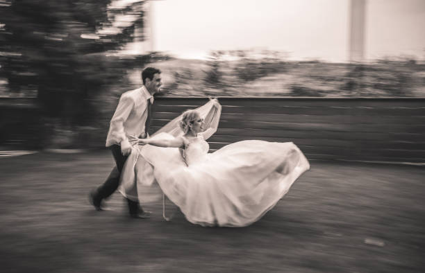 Young carefree newlyweds having fun while groom is pushing his bride in wheelbarrow. Blurred motion.