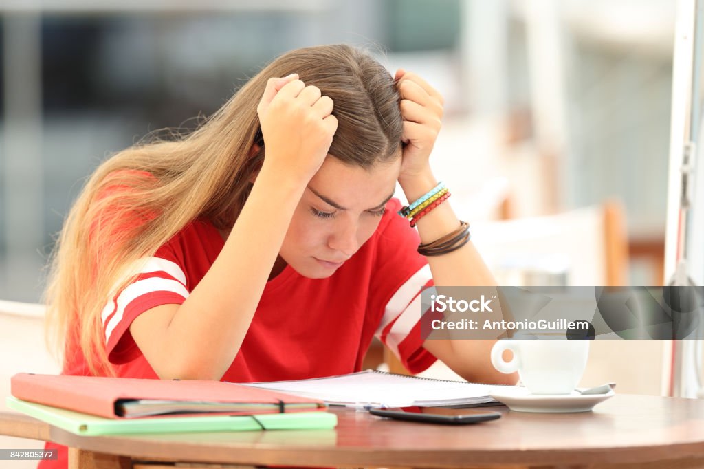 Frustrated student trying to understand notes in a bar Single frustrated student girl trying to understand notes sitting in a bar Emotional Stress Stock Photo