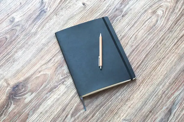 Photo of Closed planner with pen is on a wooden desk.