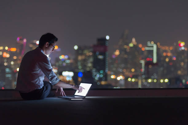 uomo d'affari che lavora fino a tardi con il computer portatile sul tetto - roof men business city foto e immagini stock