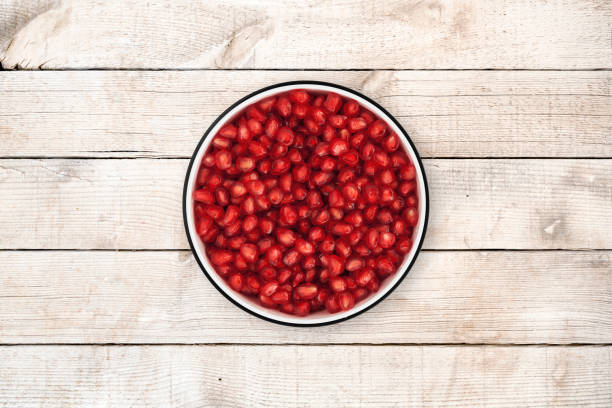 Pomegranate seeds in a circle bowl on a rustic old wood background, shot from directly above.