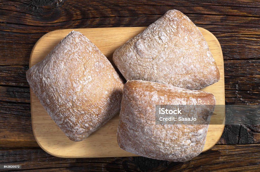 Loaves of bread ciabatta Small loaves of bread ciabatta on cutting board on dark wooden table, top view Baked Stock Photo