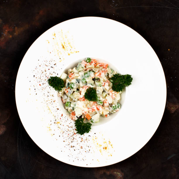 Olivier Russian Salad Traditional Russian Salad Olivier with Boiled Chicken Meat, Eggs and Vegetables Decorated with Parsley in White Plate on Dark background. Top View laurence olivier photos stock pictures, royalty-free photos & images