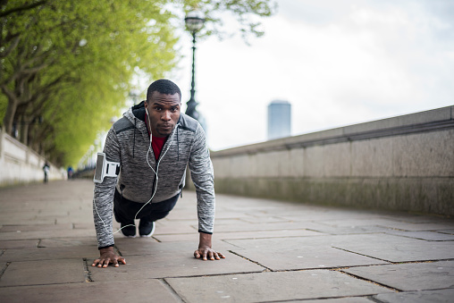 Active young African American man doing push ups on city promenade by the river